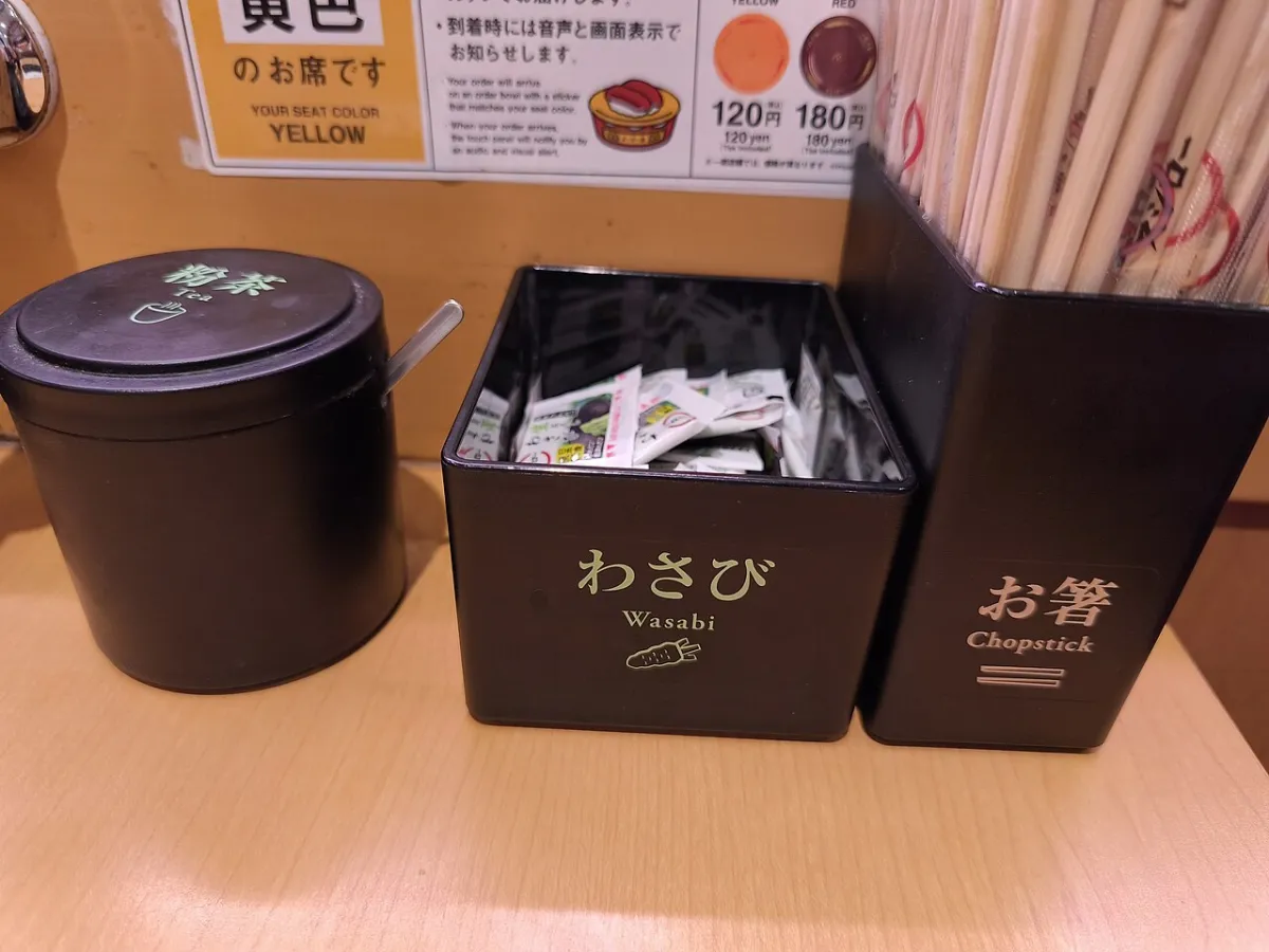 Sushiro table setup in Japan with self-serve green tea powder, wasabi packets and plate prices from 120 yen