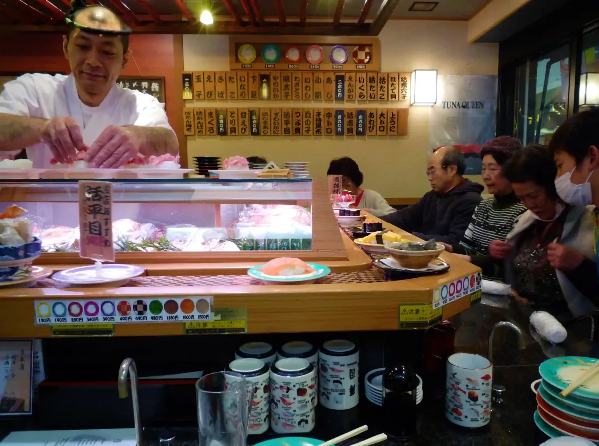 Tourist couple laughing while eating sushi from a conveyor belt at a busy Tokyo restaurant